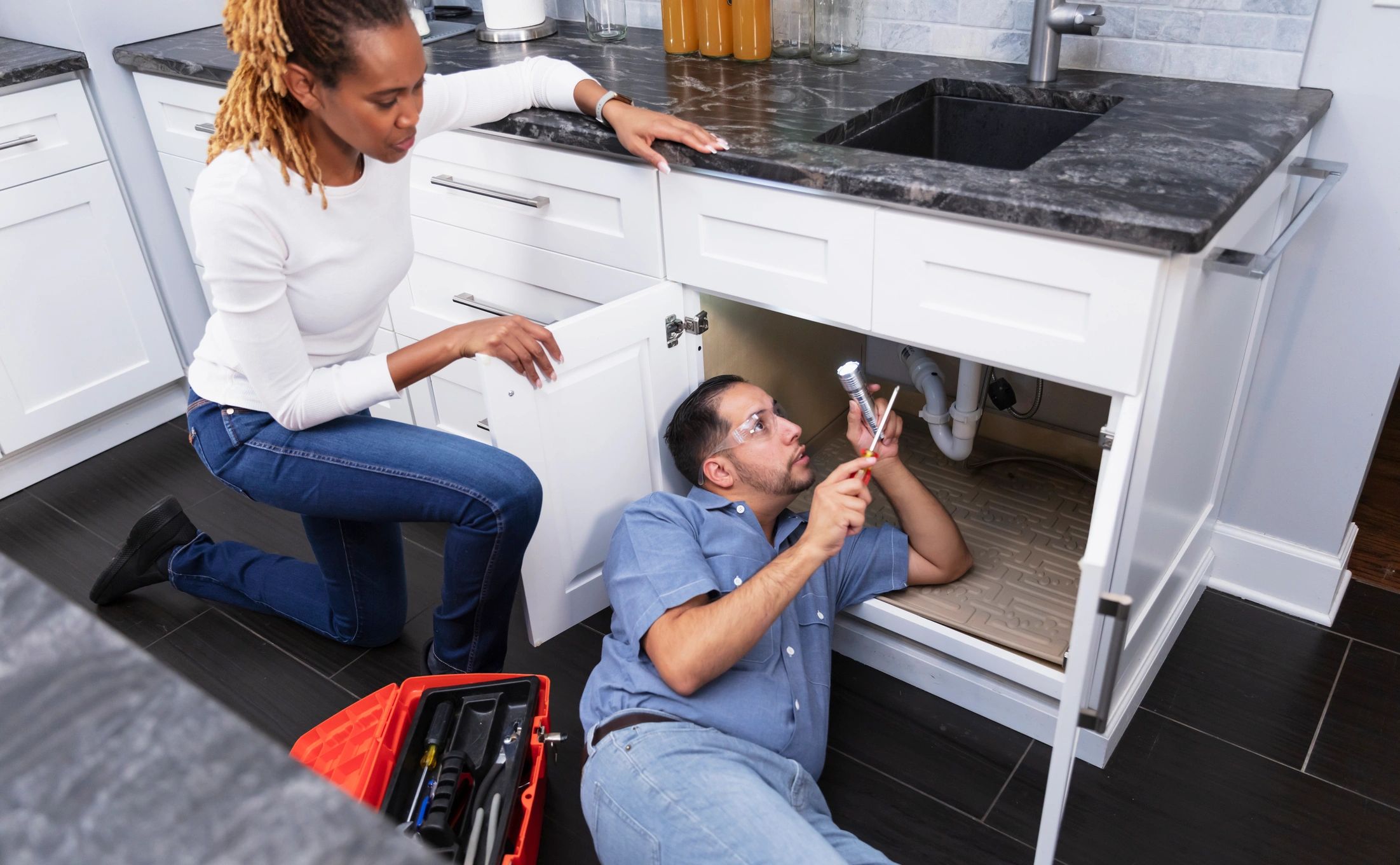 Plumber inspecting under a kitchen sink while speaking with a homeowner